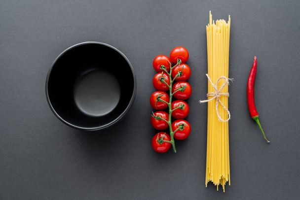 Bovenaanzicht van kom bij verse groenten en ongekookte pasta op zwarte ondergrond  - Foto, afbeelding