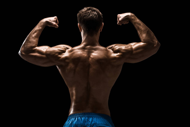 Строгий атлетичный мужчина, позирующий мышцами спины, трицепсы на черном фоне. Студия на черном фоне. - Фото, изображение