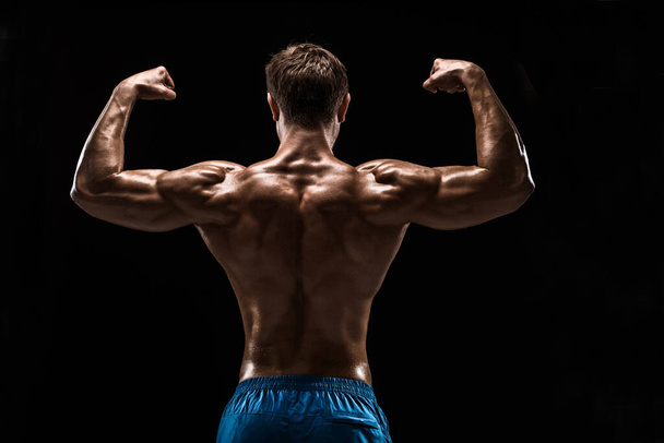 Ισχυρός αθλητικός άνθρωπος Fitness μοντέλο ποζάροντας τους μυς της πλάτης, τρικέφαλος πάνω από μαύρο φόντο. Στιγμιότυπο σε μαύρο φόντο. - Φωτογραφία, εικόνα