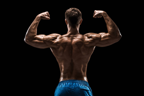 Ισχυρός αθλητικός άνθρωπος Fitness μοντέλο ποζάροντας τους μυς της πλάτης, τρικέφαλος πάνω από μαύρο φόντο. Στιγμιότυπο σε μαύρο φόντο. - Φωτογραφία, εικόνα