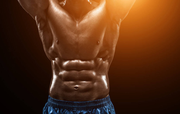 Muskulöse und fitte junge Bodybuilder Fitness männliches Modell posiert vor schwarzem Hintergrund. Studioaufnahme auf schwarzem Hintergrund. mit Sonneneruption. Nahaufnahme - Foto, Bild