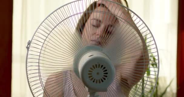 Žena sedí poblíž rotačního větráku v proudu chladného vzduchu v horké místnosti v létě. - Záběry, video