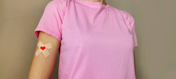 Woman in pink T-shirt hand taped with patch with red heart after giving blood . Blood donor ship - Foto, Imagem