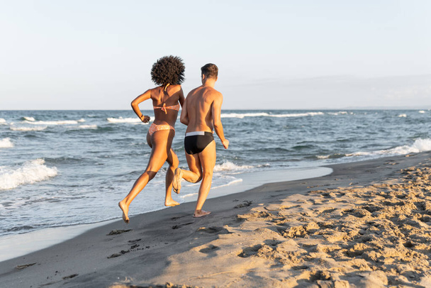 Ευτυχισμένο νεαρό ζευγάρι τρέχει στην παραλία στο ηλιοβασίλεμα αγαπώντας ζευγάρι με τα πόδια στην παραλία διακοπές Οι άνθρωποι στην παραλία το καλοκαίρι παραλία καλοκαιρινές διακοπές διασκεδαστικό ζευγάρι - Φωτογραφία, εικόνα
