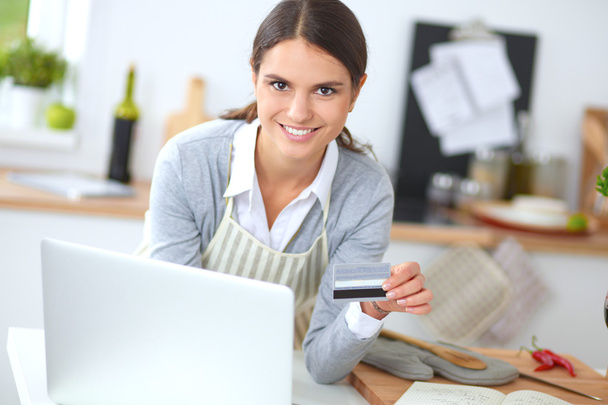 Smiling woman online shopping using computer and credit card in kitchen - Zdjęcie, obraz