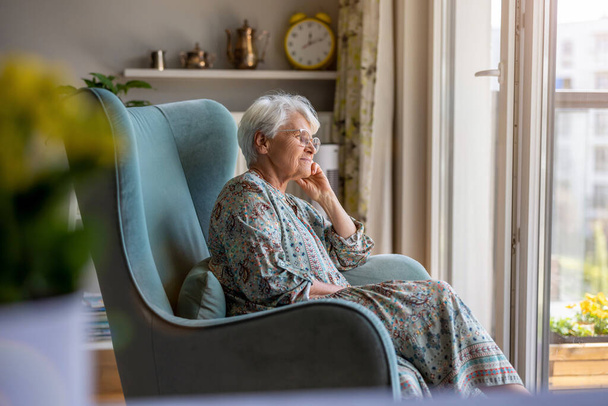 Oudere vrouw zit in een fauteuil in haar huis - Foto, afbeelding