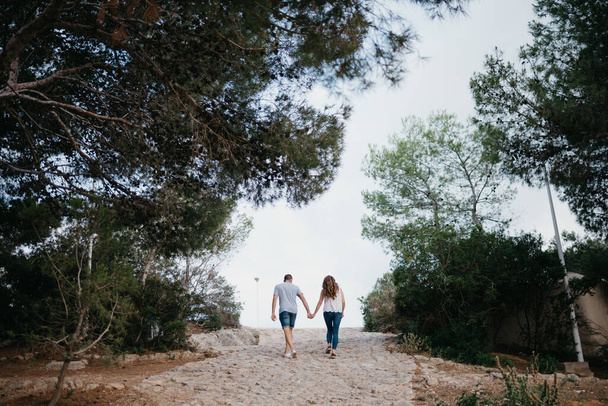 Una foto de detrás de un hombre hispano y una mujer morena que están paseando por el parque en España por la noche. Un par de turistas en una cita al atardecer en Valencia. - Foto, Imagen