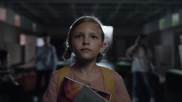 Portrait of tensed little girl walking lively hallway holding books. Focused blonde child going dark corridor on school break alone looking ahead. Stressed frightened pupil worrying about first day. - Footage, Video