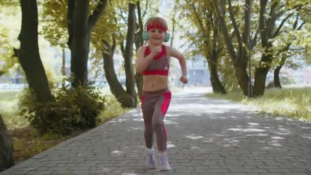 Atletische fitness sport loper peuter meisje training marathon lopen, luisteren muziek in hoofdtelefoon. Trainen cardio buiten in het park 's morgens. Kind met een gezonde levensstijl. Actieve kinderjogger - Video