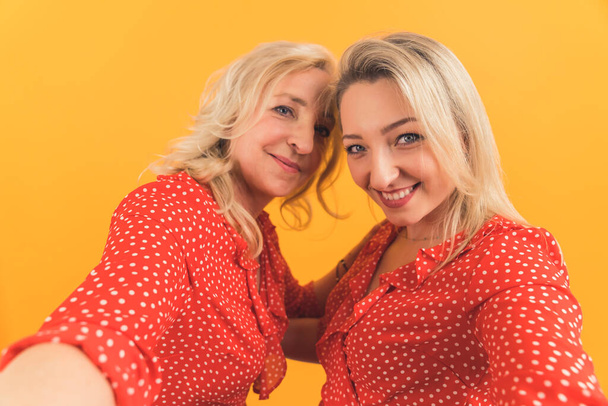 laisse prendre un selfie - deux femmes heureuses européennes blondes prenant un selfie moyen gros plan studio tourné fond orange. Photo de haute qualité - Photo, image