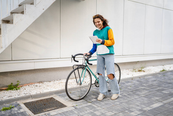 One woman young adult caucasian female walking by the university building holding bicycle and digital tablet in day real people copy space full length side view - Foto, Imagen