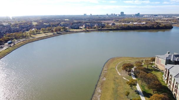 Arka planda Las Colinas, Irving, Teksas şehir merkezindeki hava manzaralı nehir kenarı apartmanı. Beton kaldırımlı çok katlı kiralık kompleksi, renkli sonbahar yaprakları, güneşli mavi gökyüzü. - Fotoğraf, Görsel