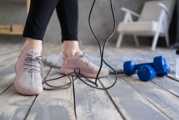 woman feet on the floor after exercising with dumbbell and jump rope at home. Concept of healthy and sport - Фото, изображение