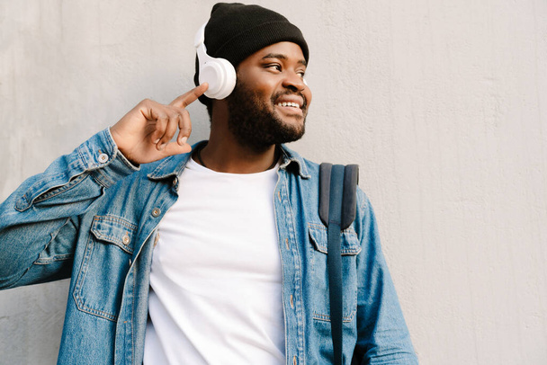 Black young man smiling and listening music with headphones outdoors - 写真・画像