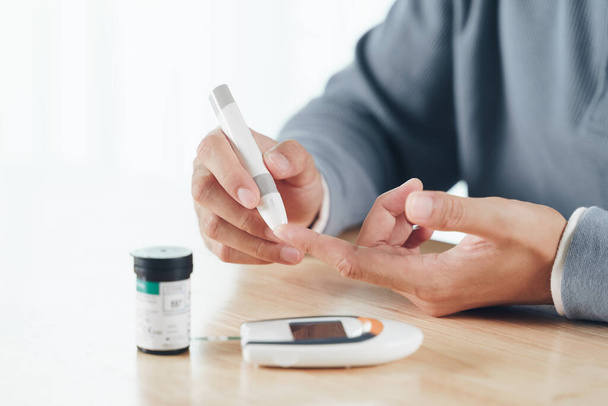 Asian man using lancet on finger for checking blood sugar level by Glucose meter, Healthcare and Medical, diabetes, glycemia concept - Photo, image