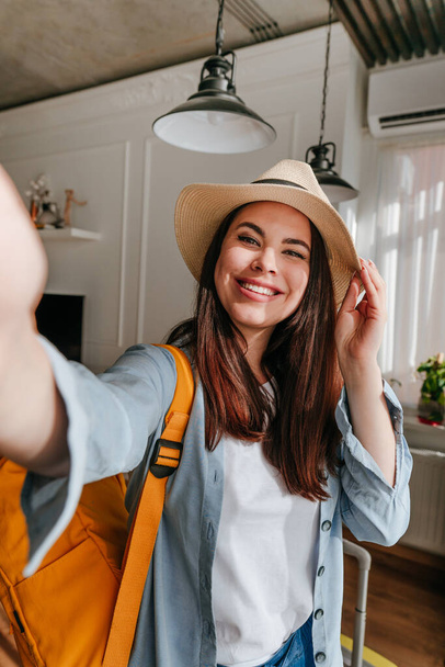 Genç kadın blogcu, bir otel odasında tatilin tadını çıkarırken akıllı telefon kullanarak selfie çekiyor. Çantalı ve sırt çantalı turist çevrimiçi oda turu yapıyor.. - Fotoğraf, Görsel