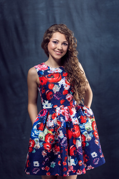Молода красива дівчина з макіяжем в кольоровій сукні позує в студії посміхаючись в студії
 - Фото, зображення