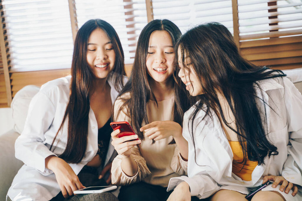 Belle donne asiatiche utilizzano smartphone social media insieme seduti sul divano in una stanza accogliente - Foto, immagini