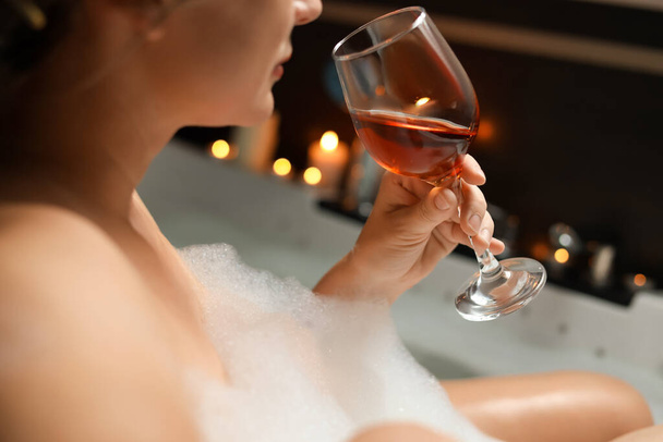 Woman drinking wine while taking bubble bath, closeup. Romantic atmosphere - Zdjęcie, obraz