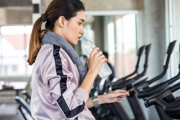 Sportfrauen trinken Wasser nach Burn-out auf dem Fahrrad in Fitnessstudio gesunder Lebensstil - Foto, Bild