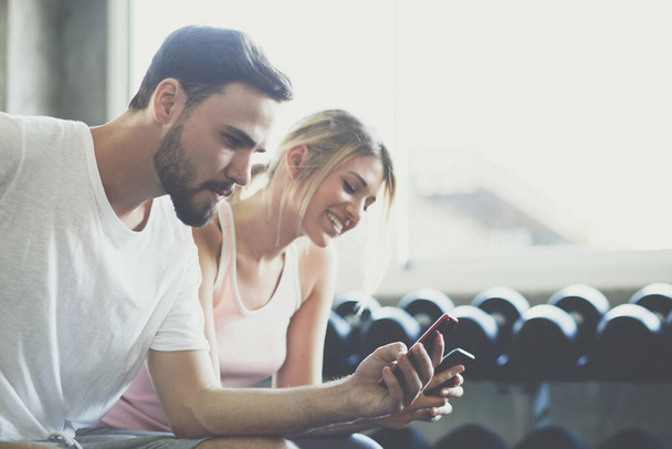 Couple of men women use smartphone talking together after working out in fitness gym - 写真・画像