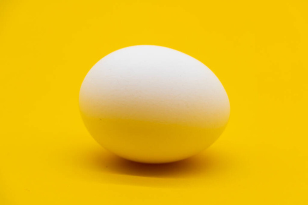 single white chicken egg isolated on yellow background. - Foto, imagen