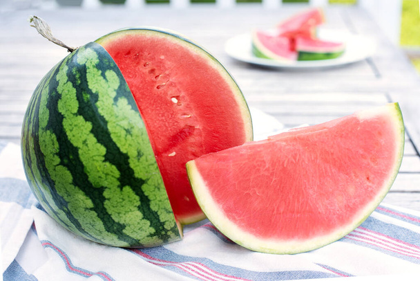 Close-up of striped watermelon and slice on wooden table outdoors, summer concept. - Fotografie, Obrázek