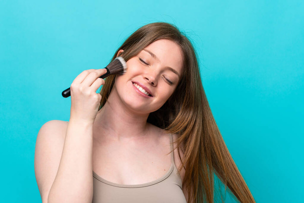 Young caucasian woman isolated on blue background holding makeup brush - Fotó, kép