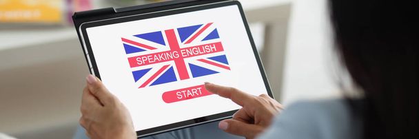 Großaufnahme einer Lady Press auf dem Tablet-Bildschirm, die online Englisch lernt. Bildungsprozess von zu Hause aus, englische Flagge auf dem Gerät. Entwicklung, Kompetenzkonzept - Foto, Bild