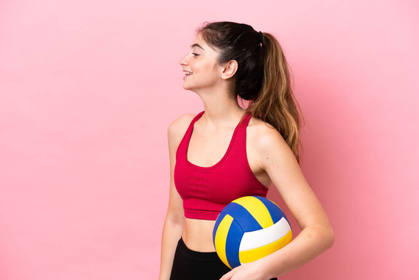 Молодая белая женщина играет в волейбол на розовом фоне смеясь в боковом положении - Фото, изображение
