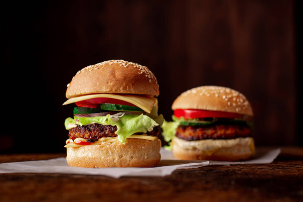 Two hamburgers on a wooden background. Big and small cheeseburger. Hamburger day. - Fotoğraf, Görsel