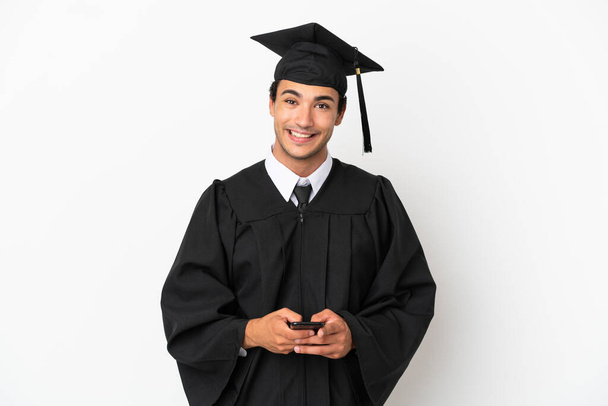 Młody absolwent uniwersytetu na odizolowanym białym tle wysyłanie wiadomości z telefonu komórkowego - Zdjęcie, obraz