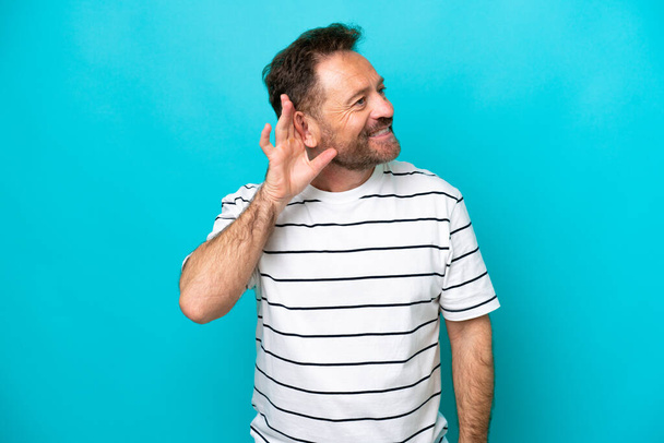 Middle age caucasian man isolated on blue background listening to something by putting hand on the ear - Photo, Image