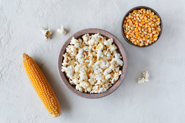 Připravený popcorn v misce, kukuřičná semínka a kukuřičné klasy na betonovém pozadí. Horní pohled - Fotografie, Obrázek