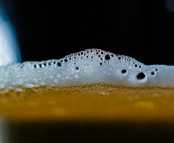 Een close-up van donker bier in een kopje met bolletjes aan de bovenkant, schuim gevormd op de top van een alcoholische drank. - Foto, afbeelding