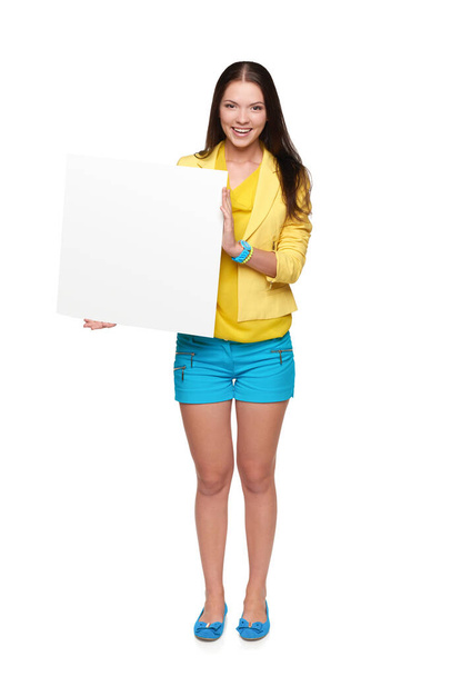 Happy girl in yellow and blue standing in full length, holding empty whiteboard, isolated - Fotografie, Obrázek