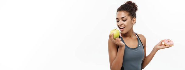 gesundes und ernährungskonzept - schöne sportliche afrikanisch-amerikanische treffen eine entscheidung zwischen donut und grünem apfel. isoliert auf weißem Hintergrund - Foto, Bild