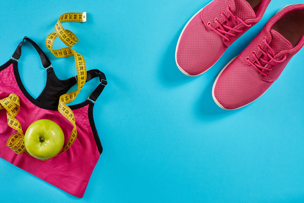 Sapatilhas com fita métrica em fundo azul ciano. Centímetro na cor amarela, tênis rosa, top esporte feminino e maçã, espaço de cópia.. Sapatos esportivos e equipamentos esportivos para forma saudável. Desportos - Foto, Imagem