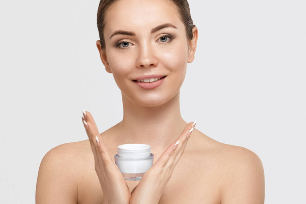 Beautiful young woman with clean fresh skin. Girl holding cream in her hand .Spa and face care - Foto, Imagem