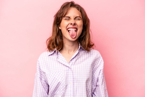 Молодая белая женщина изолирована на розовом фоне смешной и дружелюбный торчащий язык. - Фото, изображение