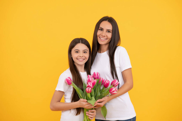 Día de las mujeres. feliz madre e hija con flores de tulipán sobre fondo amarillo. - Foto, imagen
