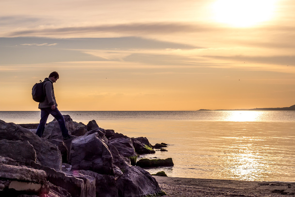 Kulkija kävelee kalliolla kohti merta, auringonnousua tai auringonlaskua
 - Valokuva, kuva