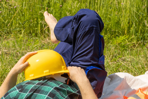 Worker relaxes lying on a meadow with a helmet and in working clothes, Concept, Work Life Balance, Balanced working and rest times in various professional groups - Photo, Image