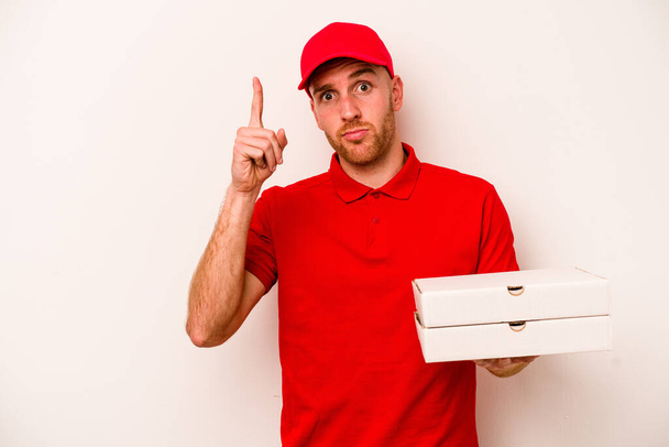 Junge Lieferung kaukasischen Mann hält Pizzen isoliert auf weißem Hintergrund zeigt die Nummer eins mit dem Finger. - Foto, Bild