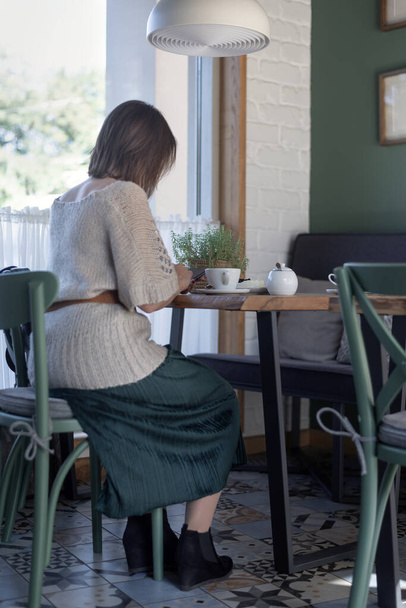 Mulher com um smartphone e se senta à mesa no café com uma xícara de café ou chá. Mulher de negócios durante o almoço. Quadro vertical - Foto, Imagem