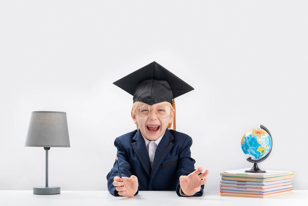 Portret fidget ucznia. Chłopiec w szkolnym mundurku i studencki kapelusz robiący śmieszne miny. Koncepcja kształcenia podstawowego - Zdjęcie, obraz