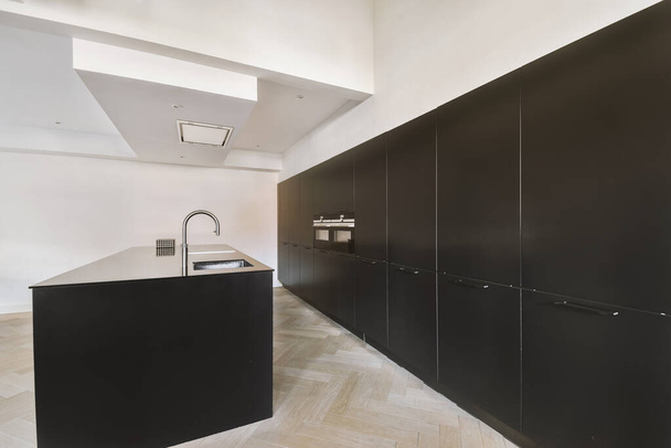 Interior da cozinha contemporânea com elegantes armários pretos e eletrodomésticos perto da área de jantar no apartamento contemporâneo - Foto, Imagem