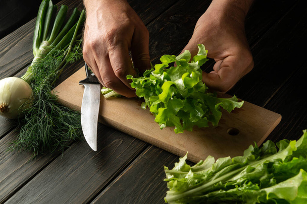 Шеф-повар готовит салат на кухонной доске. Крупный план рук повара на столе при приготовлении диетической пищи - Фото, изображение