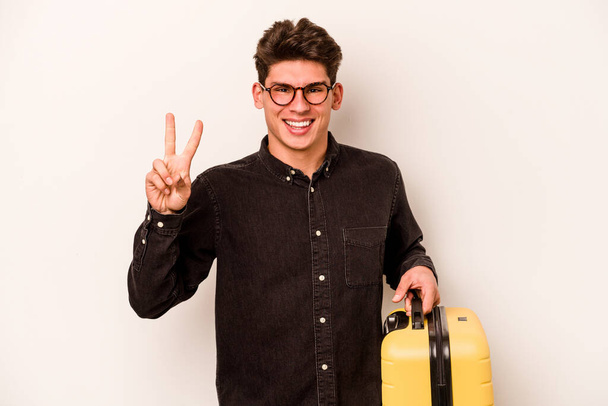 młody podróżnik kaukaski mężczyzna trzymając walizkę izolowane na białym tle pokazując numer dwa z palcami. - Zdjęcie, obraz