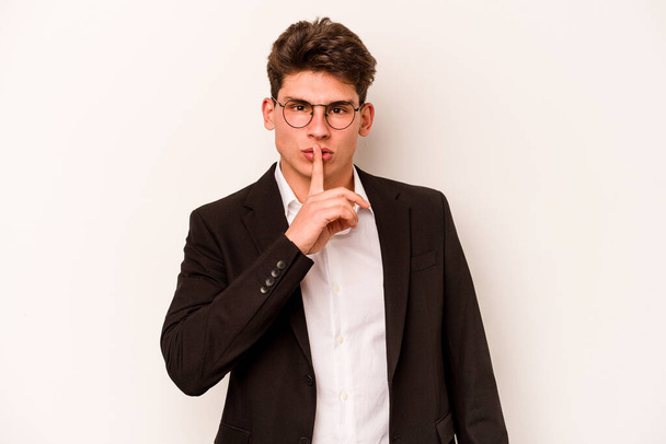 Νεαρός καυκάσιος επιχειρηματίας απομονωμένος σε λευκό φόντο κρατώντας μυστικό ή ζητώντας σιωπή. - Φωτογραφία, εικόνα